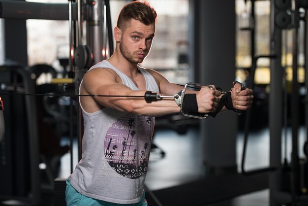 Beau bodybuilder de remise en forme musculaire faisant des exercices de poids lourds pour la poitrine sur la machine avec câble dans la salle de gym