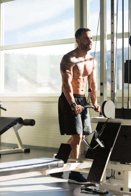 Beau bodybuilder de remise en forme musculaire faisant des exercices de poids lourds pour les triceps sur la machine dans la salle de gym