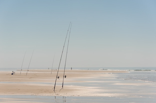 Beau bord de mer de sable avec cannes à pêche et fishman se reposer près de l'eau sous le ciel bleu