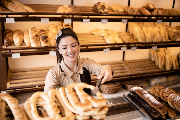 Beau boulanger souriant vendant des pâtisseries fraîches au client dans une boulangerie