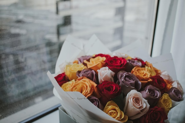 Beau bouquet d'arrangement de roses naturelles colorées avec du papier d'emballage devant la fenêtre