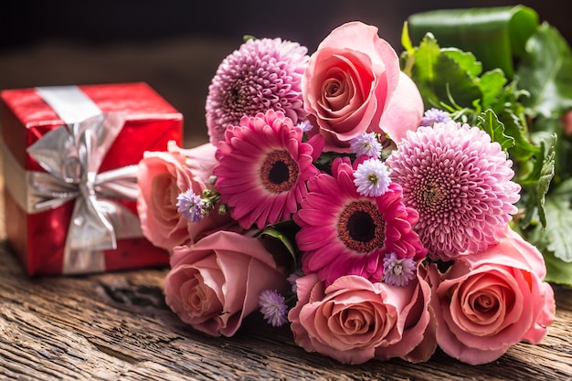 Beau bouquet de fleurs avec cadeau rouge sur table en bois.