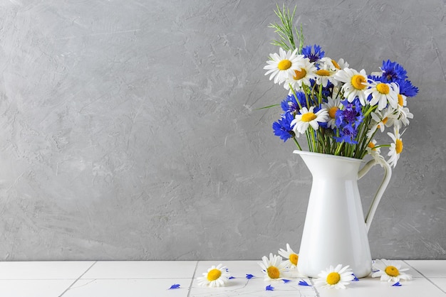 Beau bouquet de fleurs sauvages composé de fleurs de camomille blanche et de bleuets dans un vase sur fond gris journée de la femme ou fond de mariage avec espace de copie