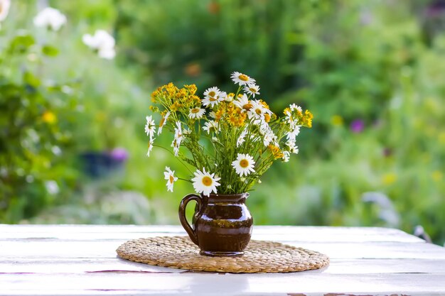 Beau bouquet de fleurs sauvages dans le contexte d'un jardin d'été Fleurs dans un vase en céramique sur un tapis en osier sur une table en bois blanc