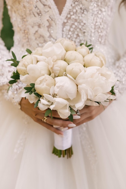 Beau bouquet de mariage blanc de pivoines entre les mains de la mariée