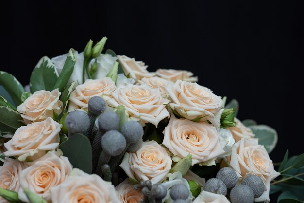 Beau bouquet de mariage composé de rose crème touffue, d’eucalyptus, de Brunei, de Pittosporum et de Lisianthus sur un mur noir.