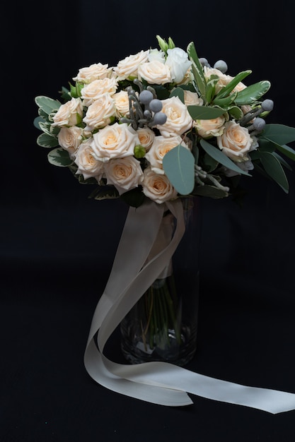 Beau bouquet de mariage composé de rose crème touffue, d’eucalyptus, de Brunei, de Pittosporum et de Lisianthus sur un mur noir.