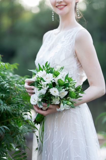 beau bouquet de mariage avec différentes fleurs sur les mains de la mariée.