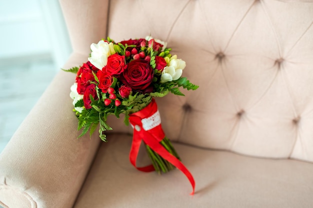 Beau bouquet de mariage tendre de fleurs de roses rouges et crème sur fond de canapé ivoire Concept de détails de mariage