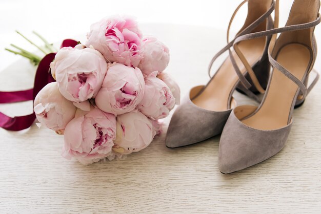 Beau bouquet de mariée de pivoines roses à côté des chaussures de la mariée