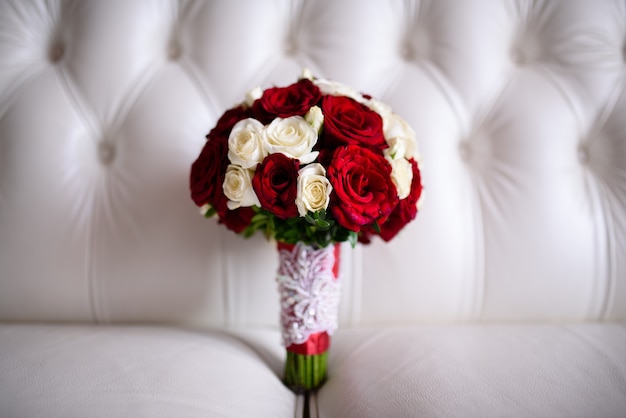 Beau bouquet de mariée de roses rouges sur un canapé blanc.