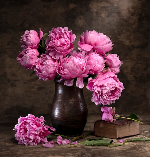 Beau bouquet de pivoines roses dans un vase et un vieux livre sur une table en bois