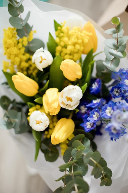 Beau bouquet de printemps avec des fleurs jaunes et bleues Mimosa delphinium tulipes et eucalyptus dans du papier d'emballage Cadeau pour la fête des mères 8 mars