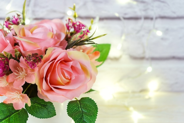 Beau bouquet romantique de roses roses sur fond de mur de briques blanches avec des lumières brillantes et un espace pour le texte. Saint Valentin, concept de mariage.