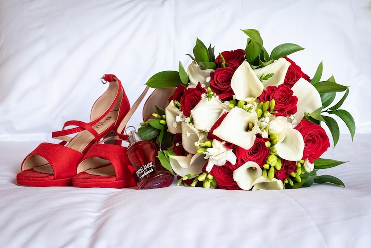 Photo un beau bouquet de roses à côté de chaussures rouges et une bouteille de parfum sur un drap blanc