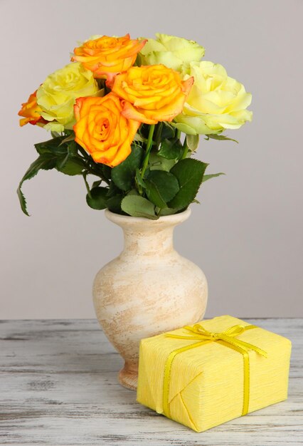 Beau bouquet de roses dans un vase avec cadeau sur table sur fond gris