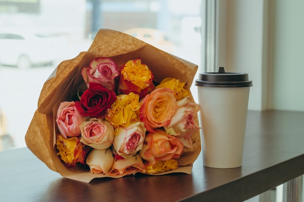 beau bouquet de roses fraîches emballées dans du papier kraft et du café pour aller tasse sur une table dans un café