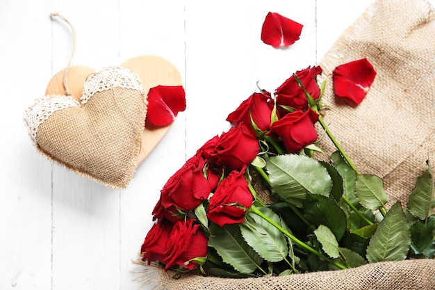 Beau bouquet de roses rouges enveloppé dans un sac avec coeur sur fond de bois