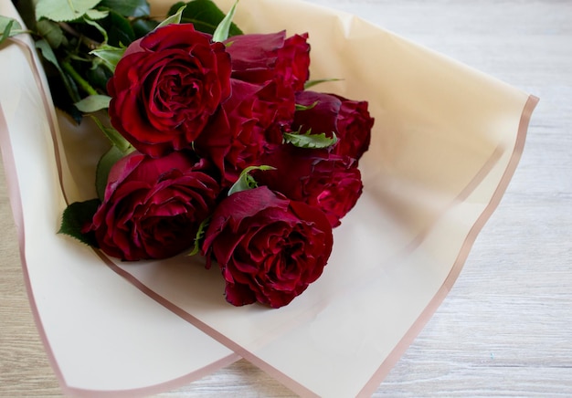 Beau bouquet de roses rouges foncées dans une pellicule plastique sur fond de bois clair gros plan avec fond