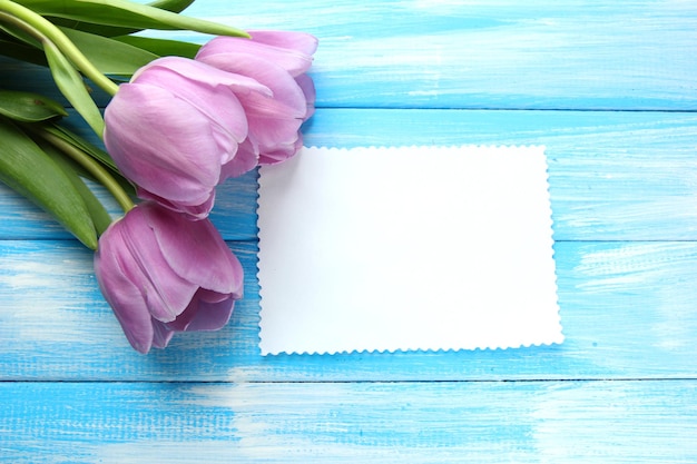 Beau bouquet de tulipes violettes et carte vierge sur fond de bois bleu