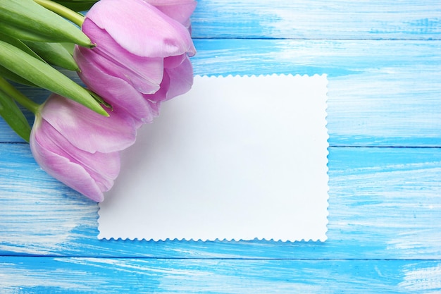 Beau bouquet de tulipes violettes et carte vierge sur fond de bois bleu