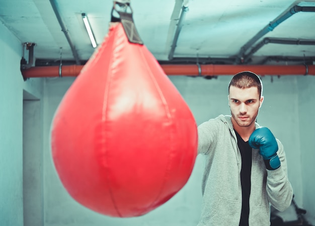 Beau boxeur masculin concentré entraîne des coups de poing à la main avec un sac de boxe.