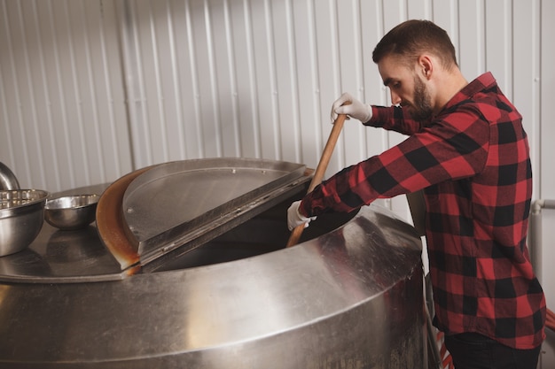 Photo beau brasseur barbu contrôlant le processus de fermentation de la bière dans son usine de bière artisanale