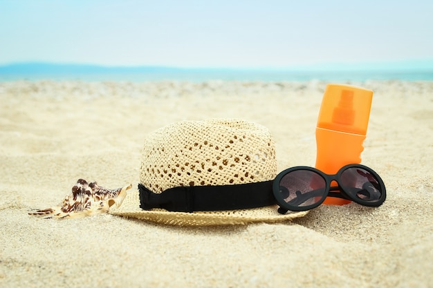 Beau chapeau avec des lunettes et de la crème sur la mer dans le sable