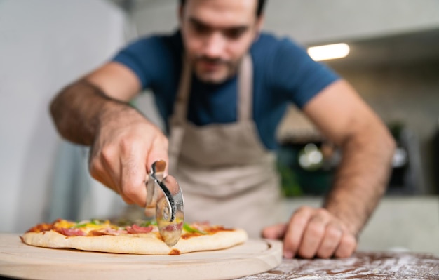 Beau chef coupe la pizza à la mozzarella de la cuisinière ou du four pour le déjeuner, le dîner, le restaurant