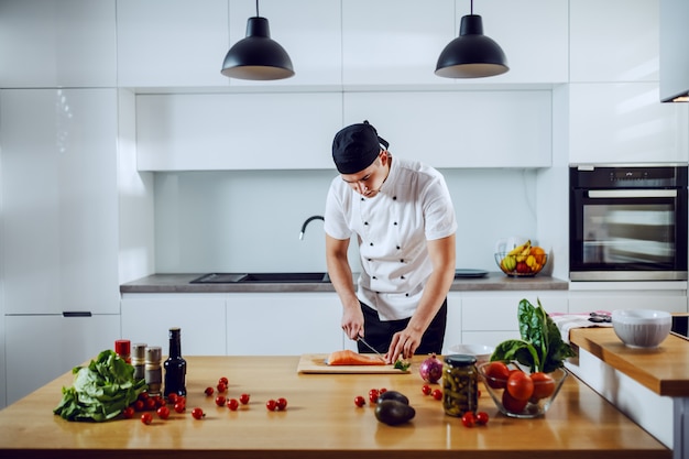 Beau chef créatif caucasien debout dans la cuisine et couper le saumon pour le déjeuner