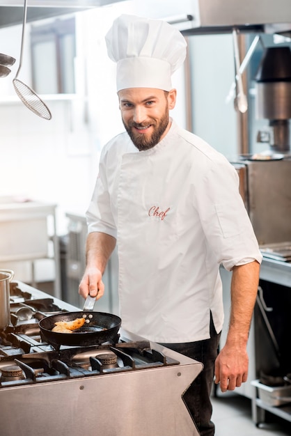 Beau chef cuisinier en uniforme faisant cuire des aliments sur la cuisinière à gaz dans la cuisine du restaurant