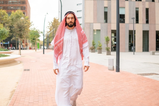 Beau cheikh arabe réussi portant des vêtements traditionnels marchant dans la rue de la ville de dubaï