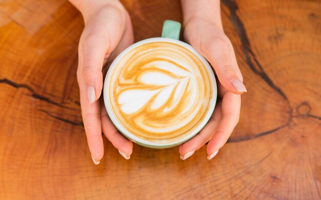 Beau coeur de modèle créé par microfoam. Concept de café et café. Cappuccino de mains féminines. Conception sur la surface du latte. Défi pour l'artiste latte. Tasse à café vue de dessus sur table en bois.