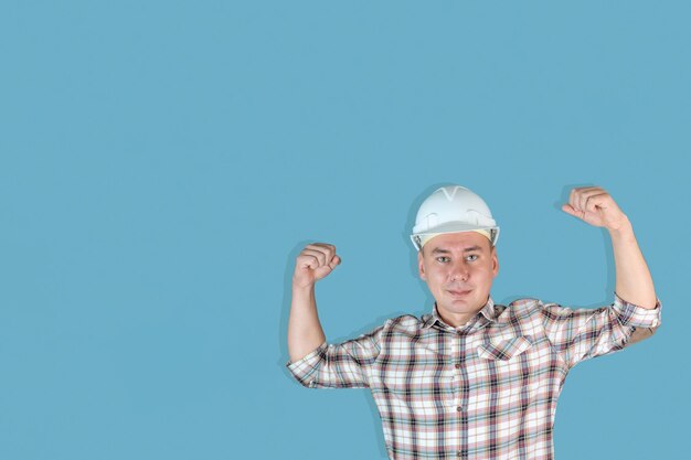 Beau constructeur d'homme fort dans un casque blanc sur fond bleu, Copyspace