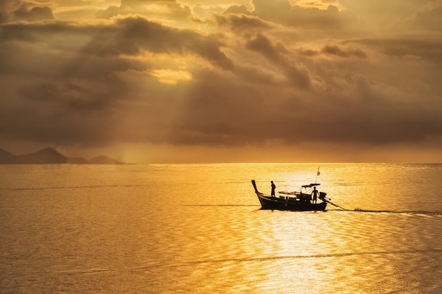 Un beau coucher de soleil doré sur la mer, pêcheur asiatique sur un bateau en bois avec l&#39;heure du coucher du soleil