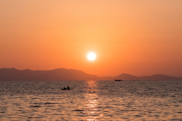 Beau coucher de soleil sur la mer avec des silhouettes de bateaux de pêche contre la côte rocheuse