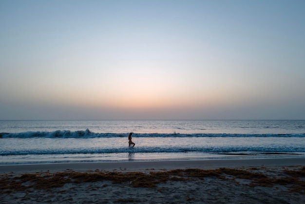 Beau coucher de soleil sur la plage avec une femme marchant sur l'eau