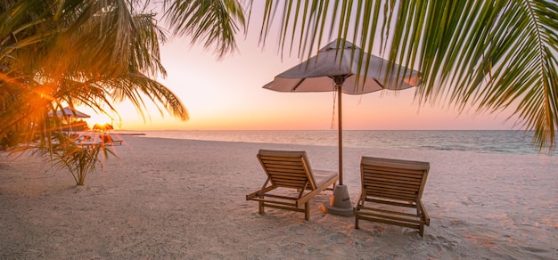 Beau coucher de soleil tropical plage mer deux chaises longues parapluie sous les feuilles de palmier Vacances d'été