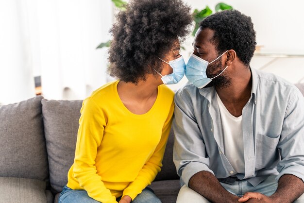 Beau couple afro-américain à la maison câlins et portant un masque protecteur pendant la quarantaine pandémique covid-19