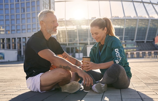 Beau couple d'âge mûr en vêtements de sport communiquant entre eux tout en buvant du café en se relaxant