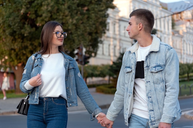 Beau couple amoureux dans des vêtements en denim se tenant la main et se regardant marchant dans la rue