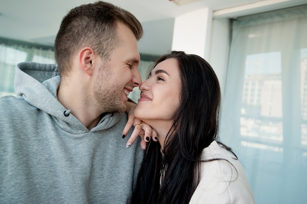 Beau couple amoureux embrassé et frotte doucement le nez. Femme brune aux cheveux longs regardant profondément dans les yeux de l'homme. Salle de lumière blanche sur fond. Un jeune couple joyeux s'est touché le nez.