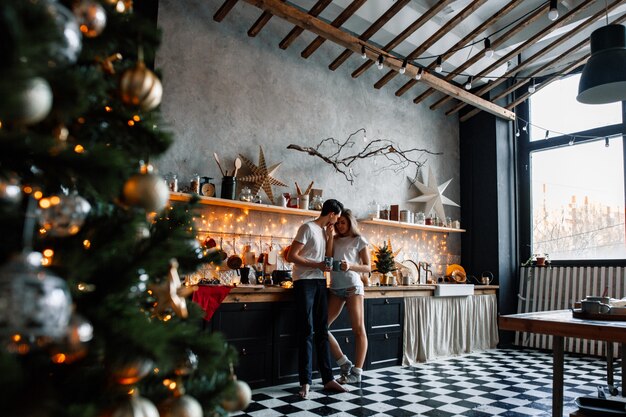 Un beau couple amoureux s'embrasse dans la cuisine, décoré pour le nouvel an ou Noël.