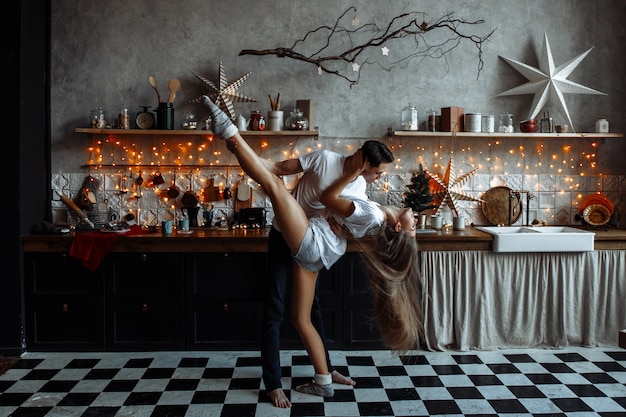 Un beau couple amoureux s'embrasse dans la cuisine, décoré pour le nouvel an ou Noël.