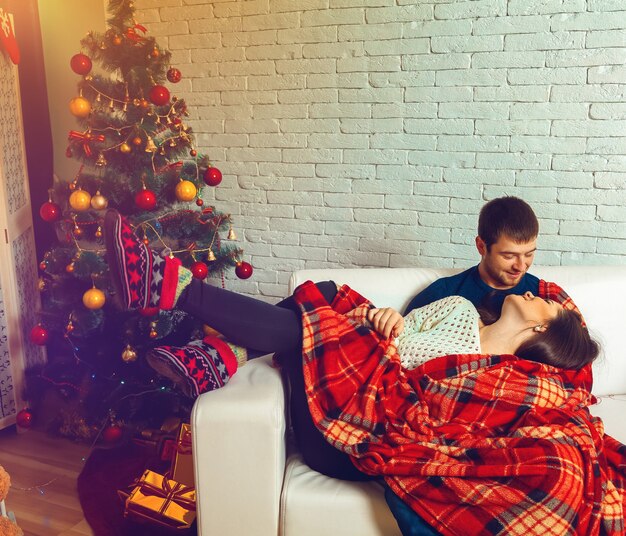 Beau couple amoureux se trouve sur un canapé enveloppé dans un plaid la veille de Noël. Nouvelle année.