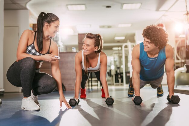 Beau couple de bonheur faisant de l'exercice au gymnase avec un entraîneur personnel féminin.