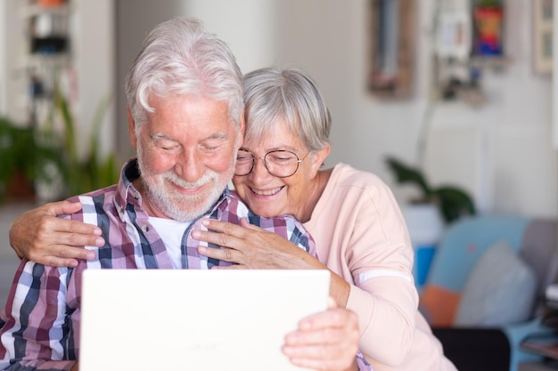 Beau couple caucasien assis à la maison naviguant sur un ordinateur portable retraités aux cheveux blancs profitant du contenu technologique et social
