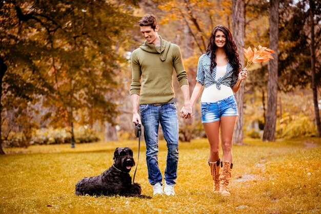 Beau couple charmant avec un schnauzer géant noir, profitant et se promenant dans le parc aux couleurs d'automne.