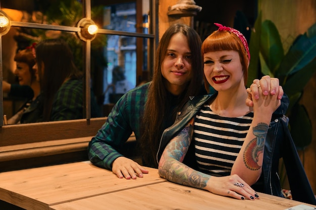 Beau couple dans un café Ils se font un câlin et elle fait un clin d'œil Il a les cheveux longs Elle est rousse Ils viennent de boire un café crémeux