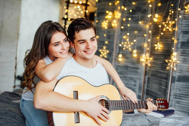 Beau couple dans leur chambre. Homme joue de la guitare